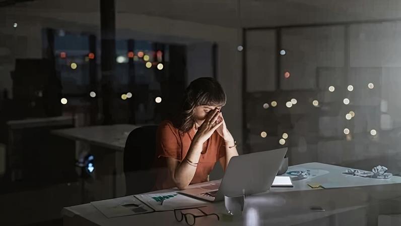 Mulher com as mãos no rosto, no escuro de um escritório, em frente ao computador