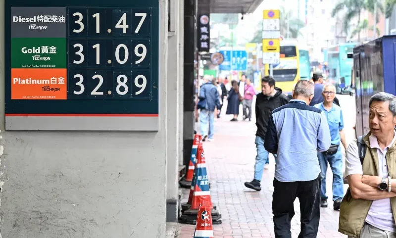 Pedestrians walk past a display with the prices in Hong Kong dollars at a gas station in Hong Kong.