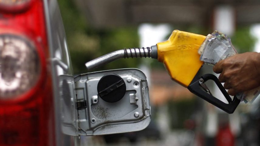 Mão com bico de combustível amarelo abastecendo carro vermelho.