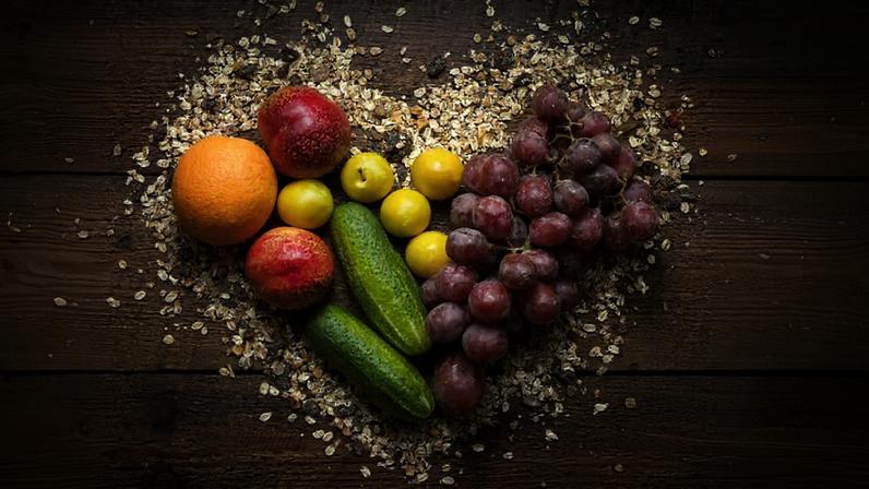 cereais, frutas e legumas frescos dispostos em uma tábua de madeira em forma de coração