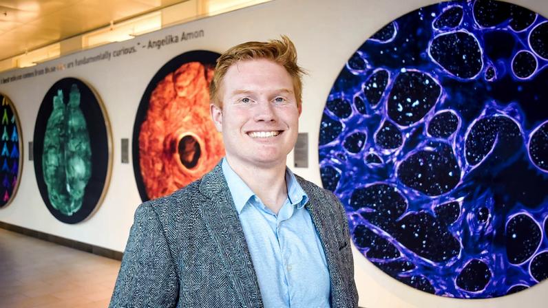Matthew Jones poses in the Koch Institute Gallery with large scientific images behind him