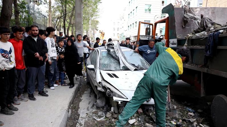 Trabalhadores removem os destroços de um carro em frente a um prédio residencial que foi alvo de um ataque no sul de Teerã em 27 de março de 2026