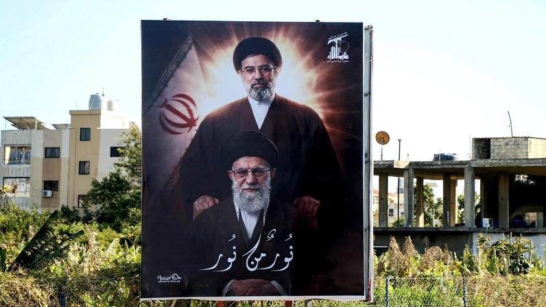 Uma fotografia mostra um cartaz com a imagem do falecido líder supremo do Irã, o aiatolá Ali Khamenei, e de seu filho, o novo líder supremo do Irã, o aiatolá Mojtaba Khamenei, exibido na entrada da cidade costeira de Tiro, no sul do Líbano