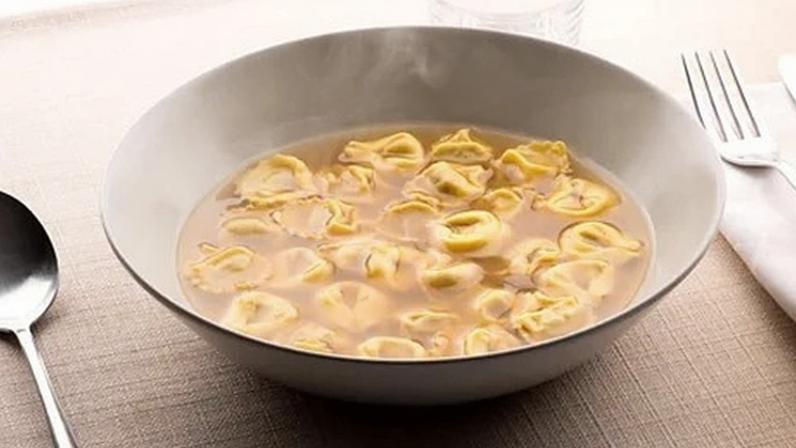 Alamy Bowl of tortellini soup in a light broth with a cutlery and a folded napkin beside it (Credit: Alamy)