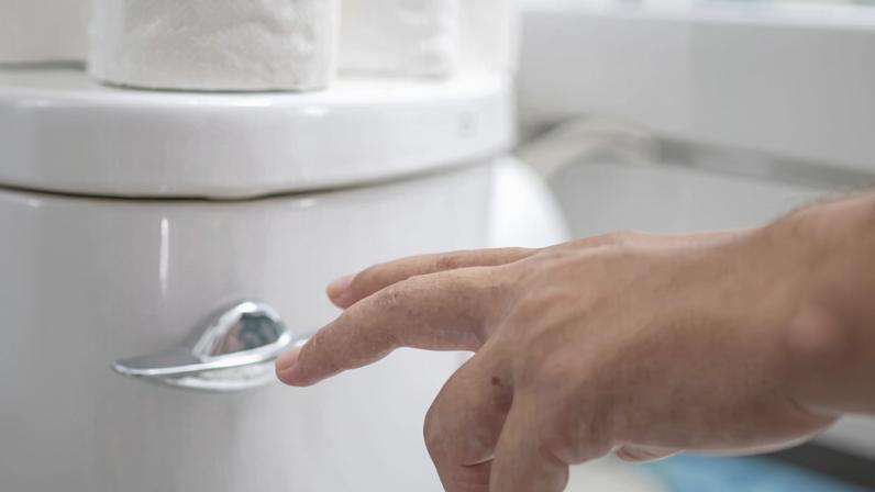 pessoa dando descarga em vaso sanitário branco com papel higiênico em cima