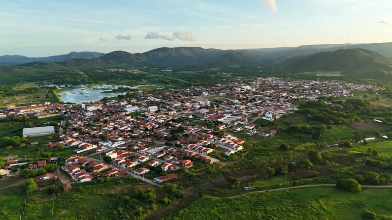 Vista aérea de pequena cidade do interior com vegetação e serras ao fundo