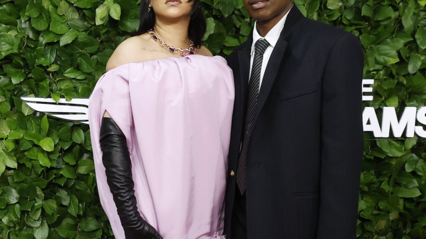 Rihanna in a pink gown with a matching hat and A$AP Rocky in a black suit pose on the green carpet of the Gotham Film Awards.