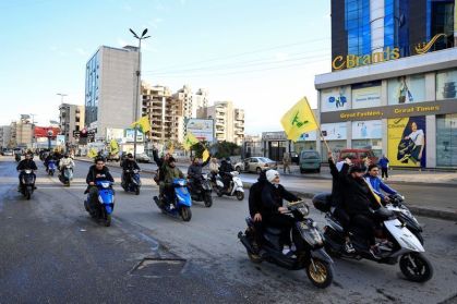 Homens carregam bandeiras do Hezbollah enquanto andam de moto, na entrada dos subúrbios ao sul de Beirute