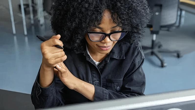 High angle view of female professional with curly hair and eyeglasses sitting at her desk. Businesswoman busy working at her desk at startup office.