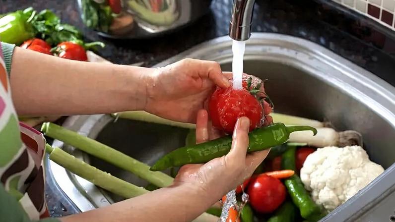 Fotografia de uma mulher lavando legumes na cozinha.