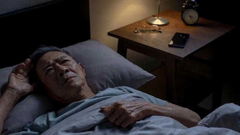 Foto de homem asiático idoso deitado na cama sem conseguir dormir.