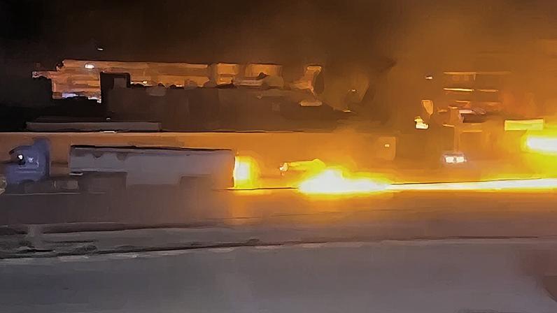 A fuel tanker truck driving with a long line of fire behind it.