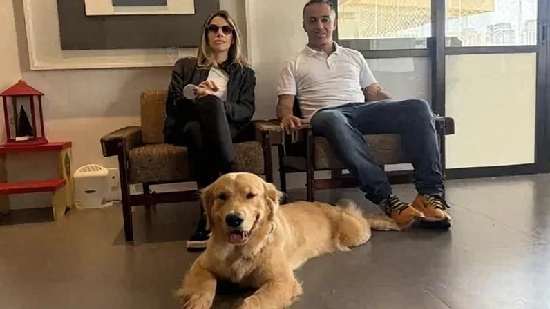 Mariana Ruiz e o treinador Glauco Lima no sofá, com a golden retriever Granola aos pés deles