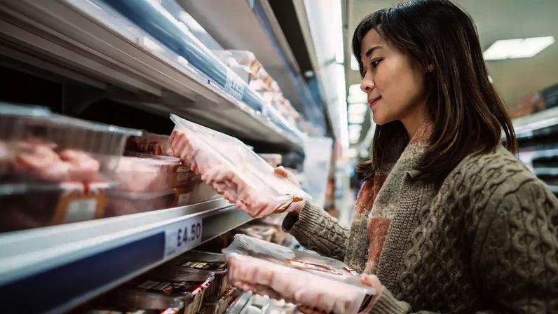 Mulher observa pacotes de frango no supermercado