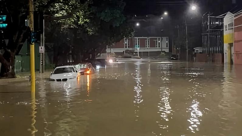 Vehicles are partially submerged along a flooded road in Wellington, New Zealand.