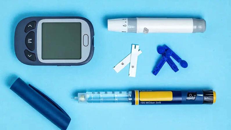 Medidor de açúcar no sangue. Glucometer, caneta de insulina, lanceta e tira de teste em um fundo azul.