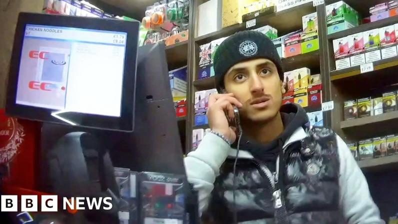 A man on his phone behind the counter of a corner shop