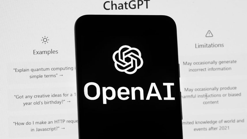 The OpenAI logo is seen on a mobile phone in front of a computer screen which displays the ChatGPT home Screen, Friday, March 17, 2023, in Boston.