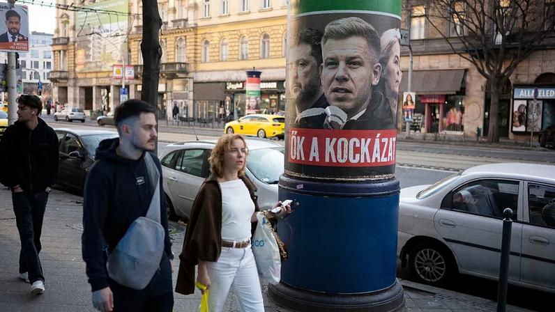 People walk next to a campaign poster which says, "They're a risk. Fidesz is the safe choice" in Budapest, Hungary, on 14 March, 2026, ahead of the parliamentary elections.