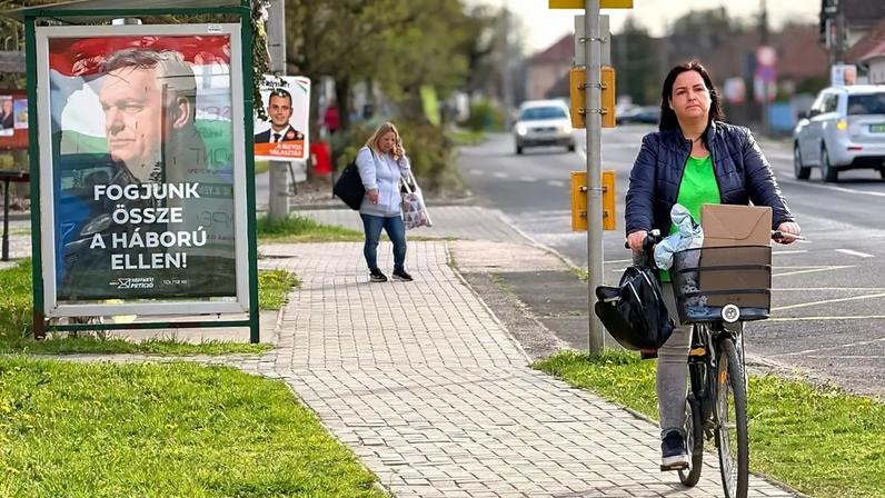 A woman rides a bicycle by a poster showing Hungarian Prime Minister Viktor Orban and the slogan "Let's stand together against the war!" in Albertirsa, Hungary, 9 April 2026