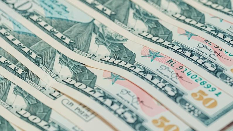 Várias notas de 50 dólares americanas dispostas lado a lado em uma superfície plana, mostrando detalhes do retrato e elementos de segurança.