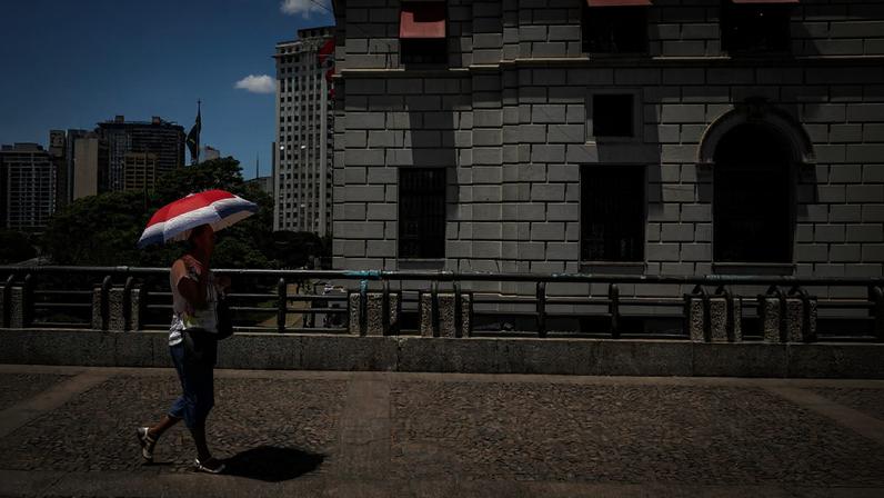Mulher se protege com guarda-sol ao caminhar pelo Viaduto do Chá, em São Paulo