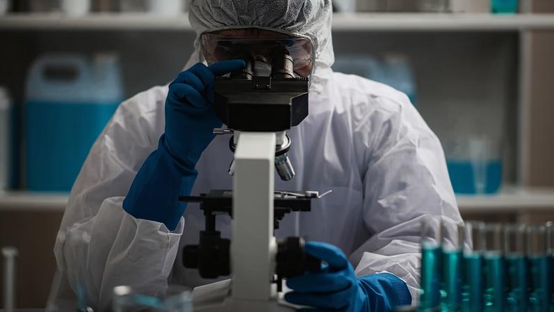 Análise de lâmina em microscópio em laboratório; técnica examina uma amostra histológica, uma biópsia, em laboratório de pesquisa sobre câncer