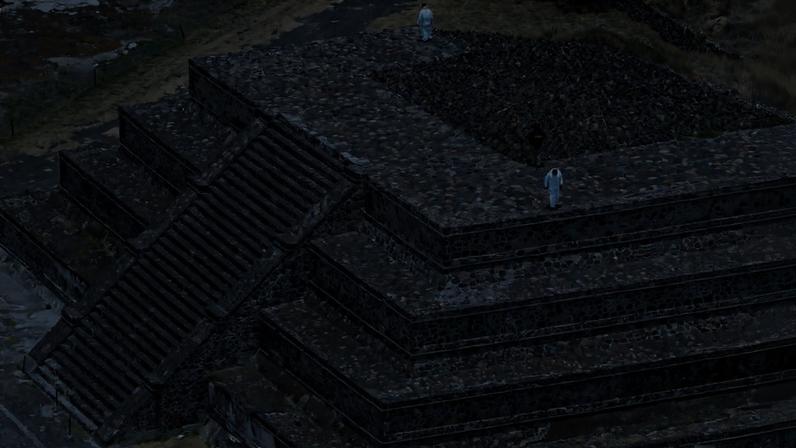 Pirâmide de pedra com quatro níveis em degraus e escadaria central larga. Três pessoas vestindo roupas claras estão no topo e nas laterais da estrutura. Vegetação seca e caminho de terra cercam o monumento.