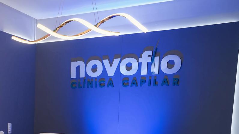 Recepção da clínica Novofio com balcão azul escuro e parede azul claro ao fundo. Buffet com pratos, taças, bolo, pães e plantas decorativas está disposto em móvel branco à esquerda. Iluminação branca destaca o ambiente limpo e organizado.