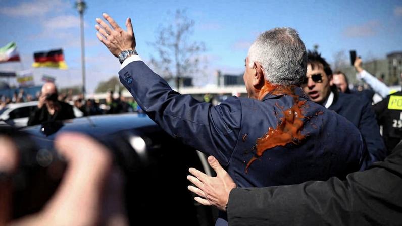 De costas, Reza Pahlavi acena para apoiadores após ser atacado com molho de tomate em Berlim