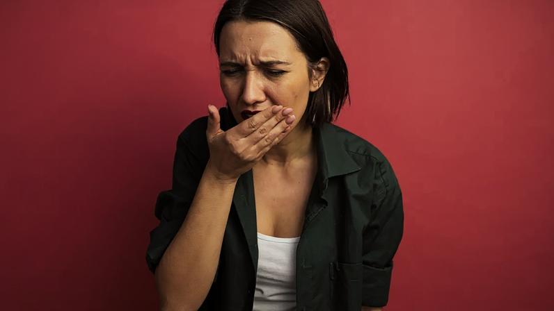 aching pretty caucasian woman puts hand on mouth isolated on pink background with copy space