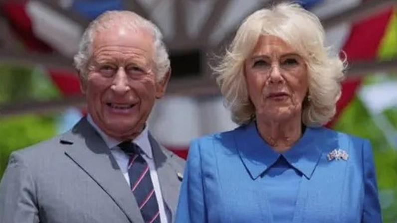Reuters King Charles and Queen Camilla look directly ahead in the sunshine during their US state visit. He is dressed in a grey suit, with shirt and tie. Camilla is wearing a blue outfit with a brooch featuring the US and British flags.