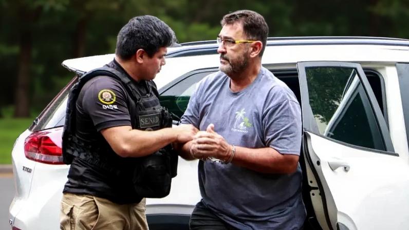 Homem com algemas na mão sendo retirado de carro por policial