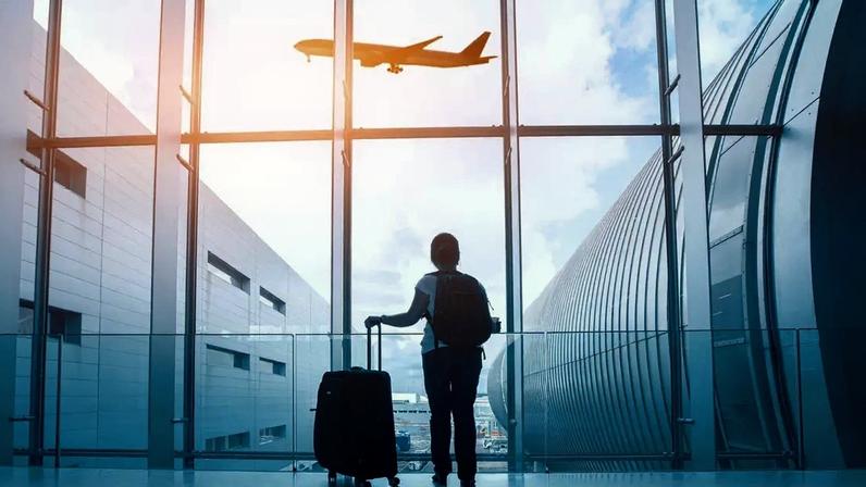 Uma mulher com bagagem está de costas para a câmera, olhando para um avião através da janela.