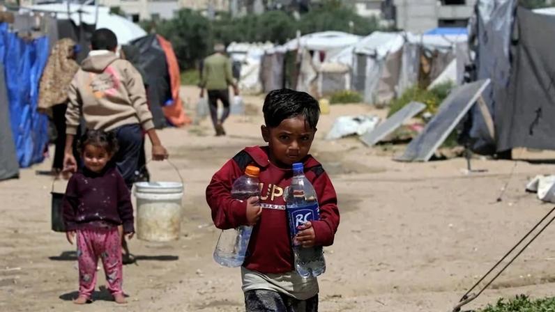Crianças buscam água potável no campo de refugiados de Bureij, no centro da Faixa de Gaza, em 28 de abril de 2026. A maioria dos 2,4 milhões de habitantes de Gaza foi deslocada, muitas vezes repetidamente, pela guerra que começou com o ataque do Hamas ao sul de Israel em 7 de outubro de 2023. Com famílias deslocadas vivendo em acampamentos de tendas, pairam sérias preocupações sobre suas condições de vida. (Foto de Eyad Baba / AFP)