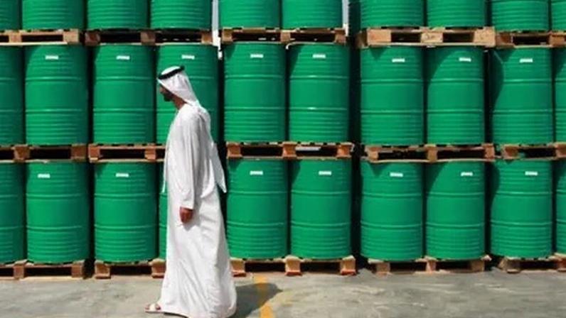 Getty Images A man wearing a long, white dishdasha walks past stacks of bright green barrels bearing "ENOC" branding.