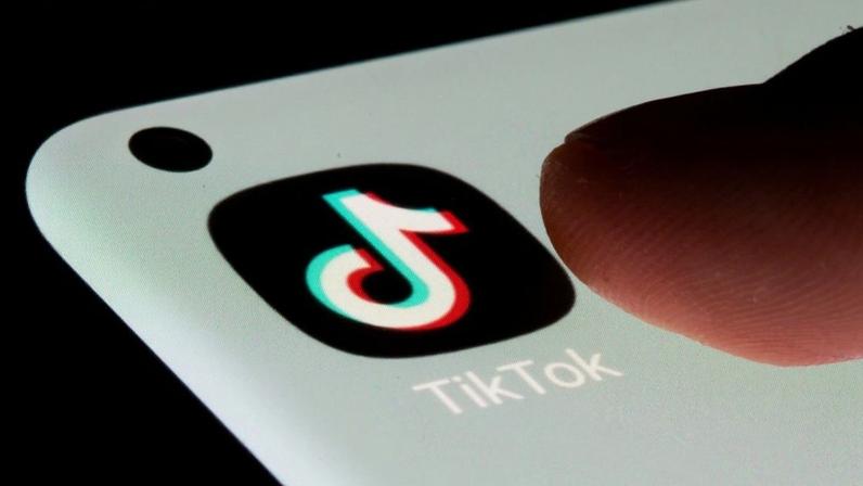 Dedo toca tela de smartphone com ícone e nome do TikTok.