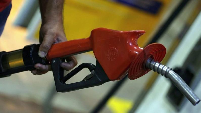 Mão segurando bico vermelho de bomba de combustível em posto.