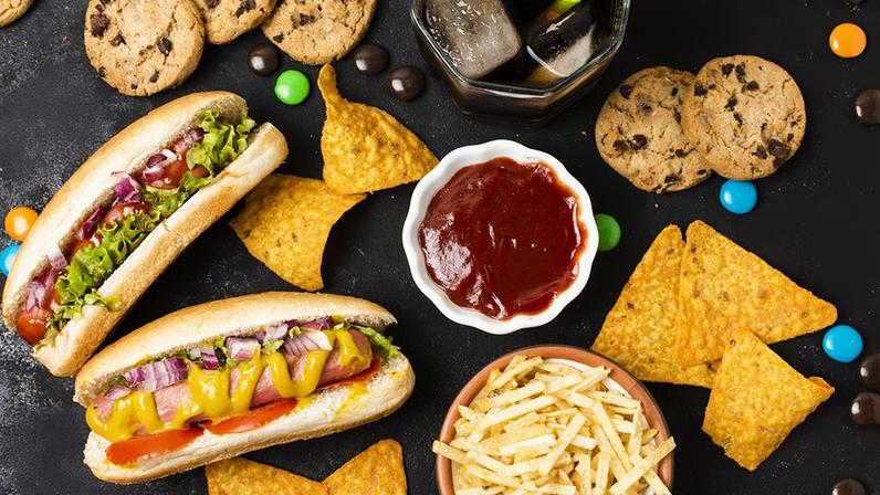 Fotomontagem mostrando uma série de alimentos considerados ultraprocessados, como hot dogs, batatas fritas, biscoitos, balas, entre outros