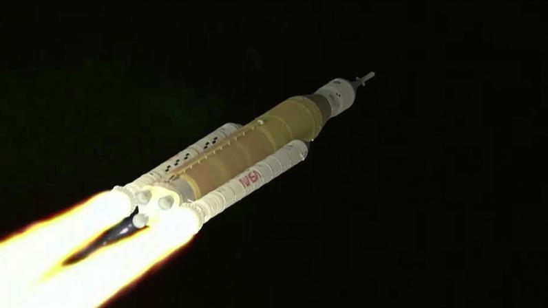 Foguete de grande porte sobe pelo espaço, soltando chamas intensas na base dos motores. Estrutura branca com tanque central laranja traz logotipo da NASA visível.