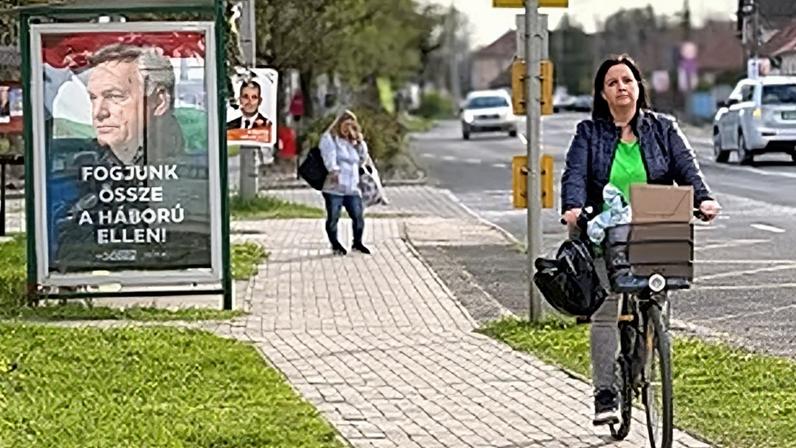 A woman rides a bicycle by a poster showing Hungarian Prime Minister Viktor Orban and the slogan "Let's stand together against the war!" in Albertirsa, Hungary, 9 April 2026