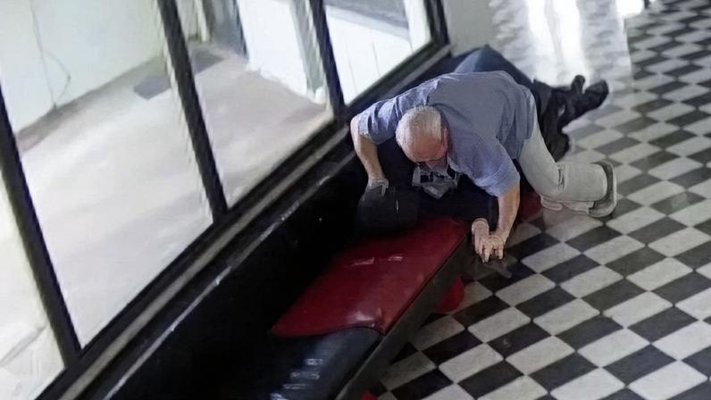 A still from CCTV footage showing a male in light coloured clothing lunging towards another male in dark clothing.