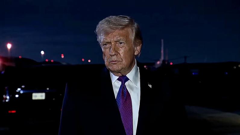 Donald Trump veste terno escuro, camisa branca e gravata roxa, posicionado ao ar livre durante a noite