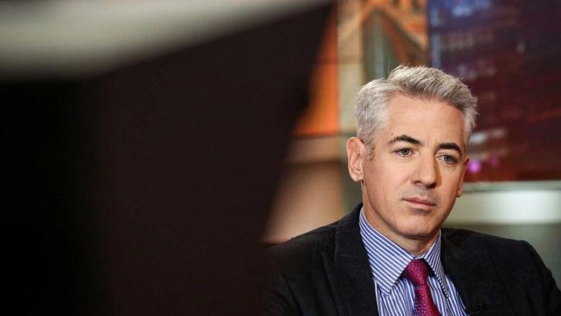 Homem com cabelo grisalho, terno escuro e gravata vermelha, olha pensativo em estúdio.