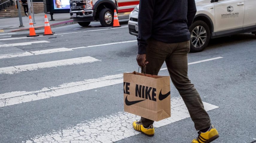 Homem atravessa faixa de pedestres com sacola Nike e tênis Adidas amarelos.
