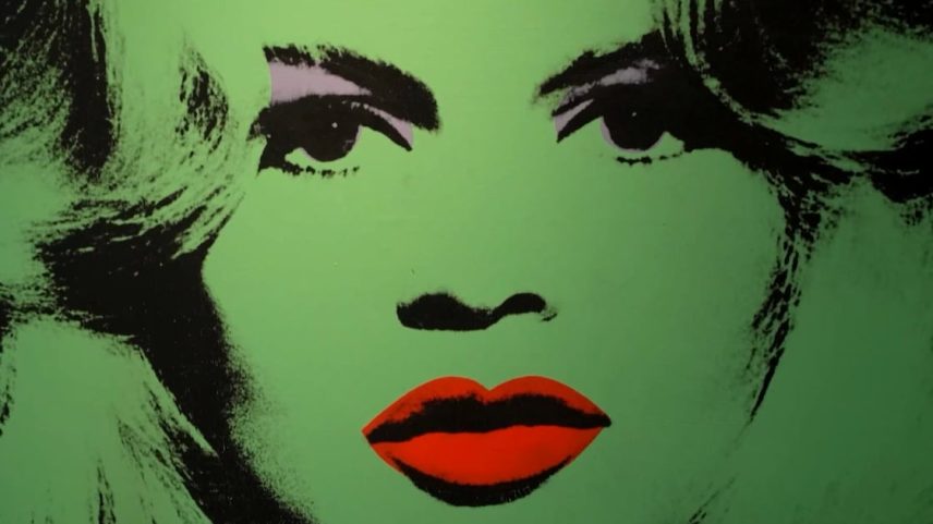 Retrato em estilo pop art de rosto humano. Pele em tom verde vibrante, lábios vermelhos intensos e detalhes pretos nos olhos, sobrancelhas e cabelo. Arte usa cores fortes e formas simplificadas, criando efeito icônico e marcante.