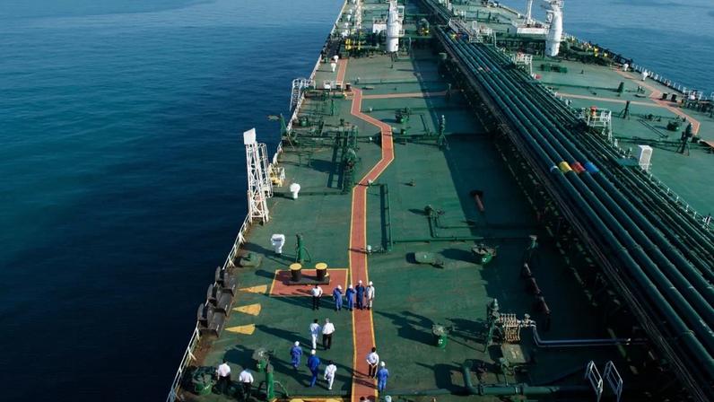 Navio-tanque no mar, com tubulações visíveis e pessoas caminhando no convés.