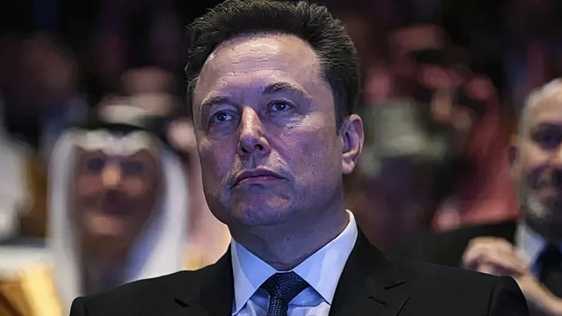 AFP via Getty Images Elon Musk, wearing a black suit, white shirt and dotted tie, looks away from the camera as he watches President Donald Trump speak at an event in Washington DC in November