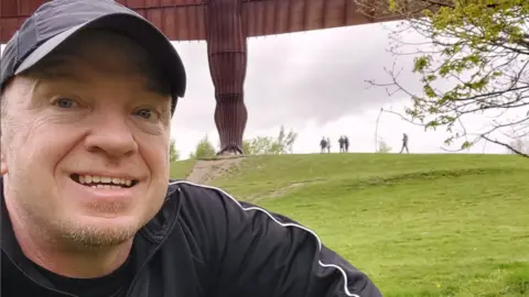Instagram/Robert Albon A man in a black baseball cap and black top smiling at the camera. He is outside and there is grass in the background.