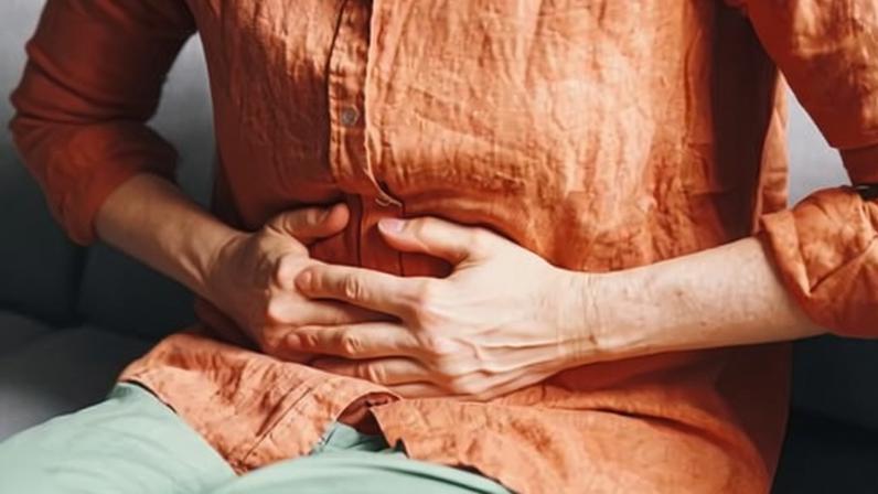 A woman sitting on a sofa and clutching her stomach in pain